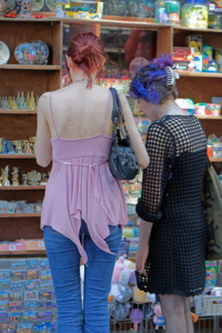 Two individuals browsing shelves filled with various souvenir items, such as miniatures, postcards, and plush